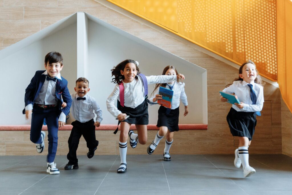 Happy school children in uniforms running energetically indoors, expressing excitement.